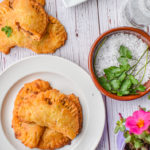 keto ground beef empanadas on white plate and on table with pink flower and round dish with salt and herbs