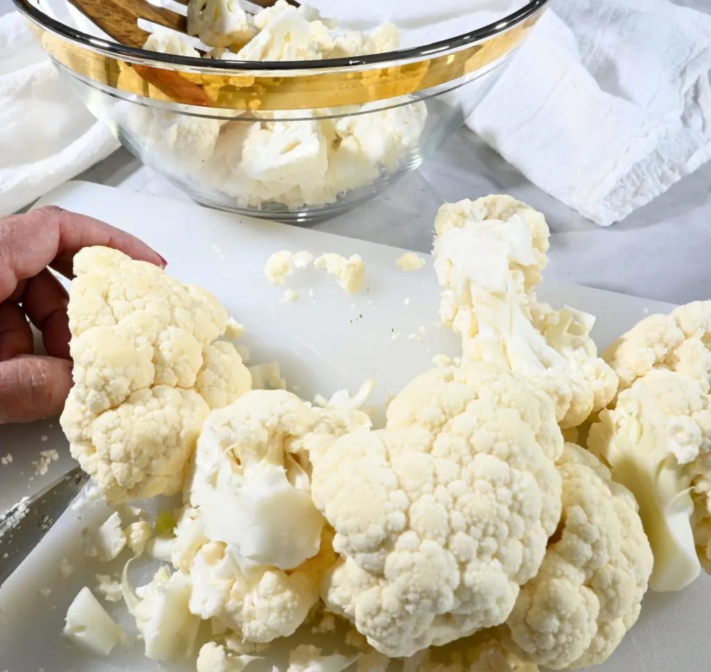 raw cauliflower being chopped on a white cutting board