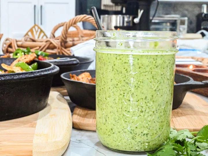 keto spicy cilantro garlic sauce in mason jar up close with cast iron skillets in background