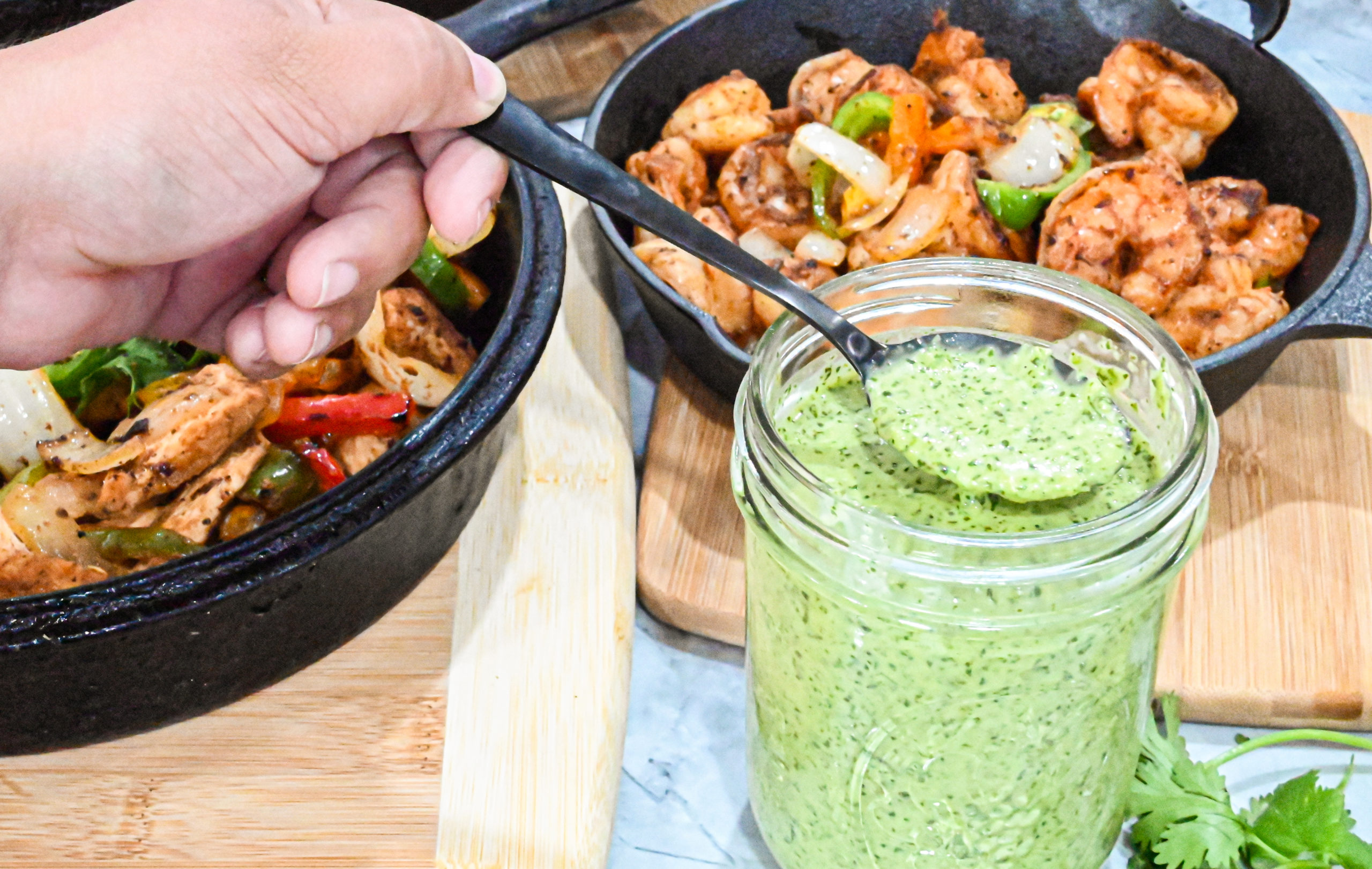 keto spicy cilantro garlic sauce in mason jar with black spoon and cast iron skillets in background