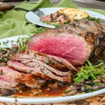 keto herb butter roast sliced and served on white platter with green cloth napkin and plater served in background