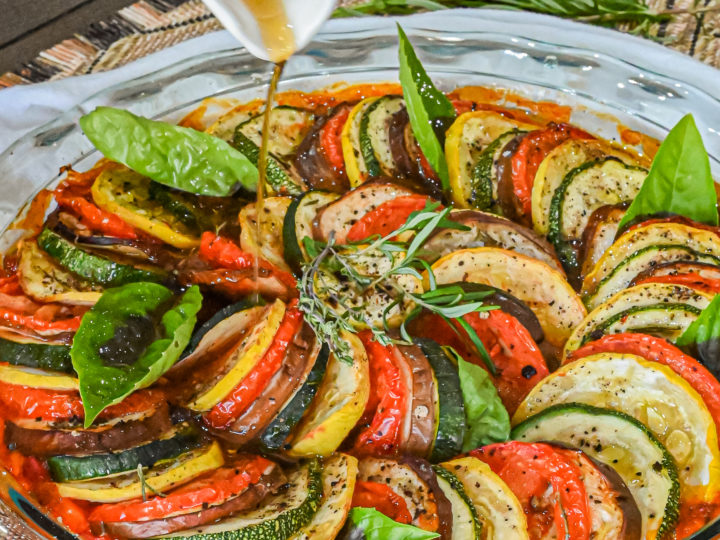 keto ratatouille in clear baking dish with vinaigrette being drizzled on top