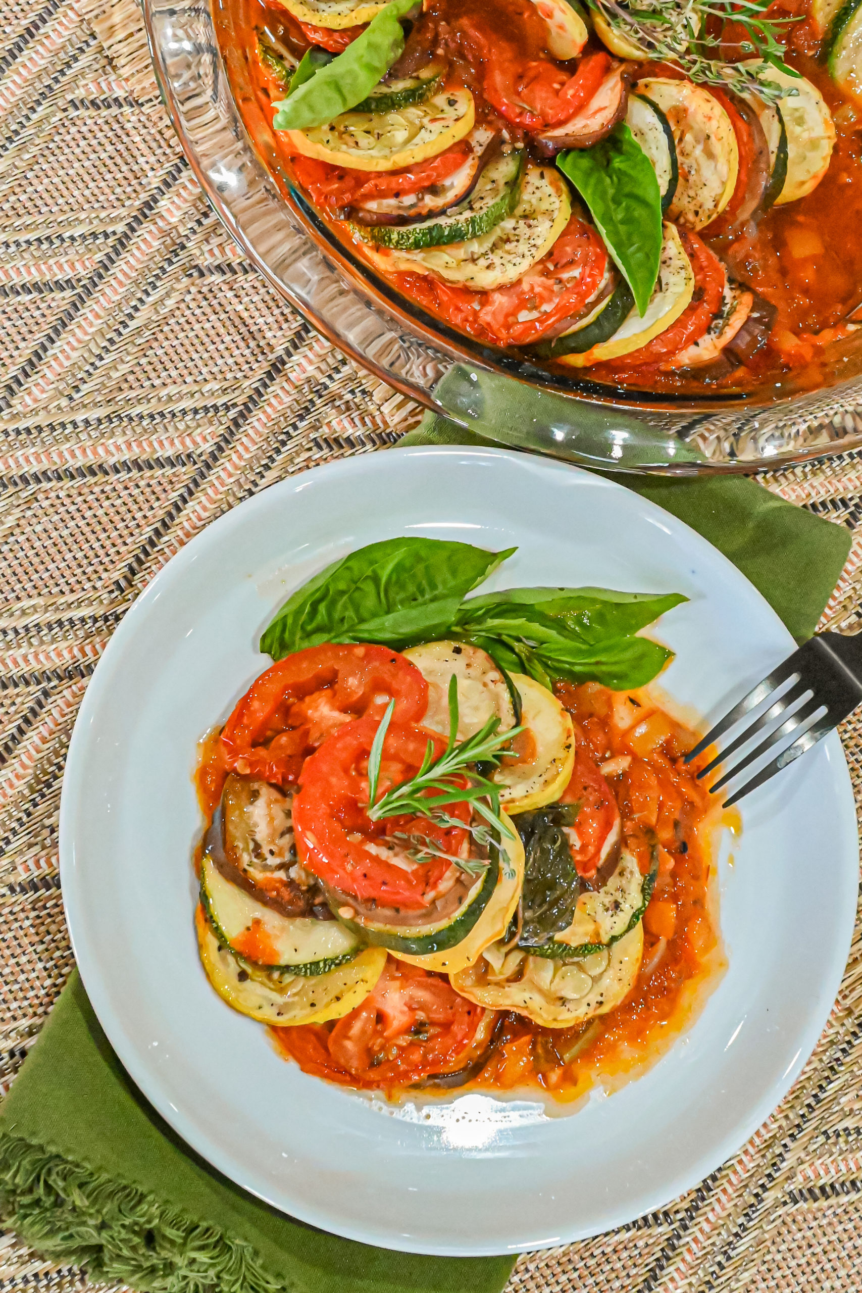 keto ratatouille served on white plate with green cloth napkin and green fork and ratatouille in baking dish in background