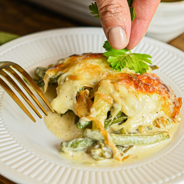 keto green bean casserole served on white plate with hand placing parsley garnish on top