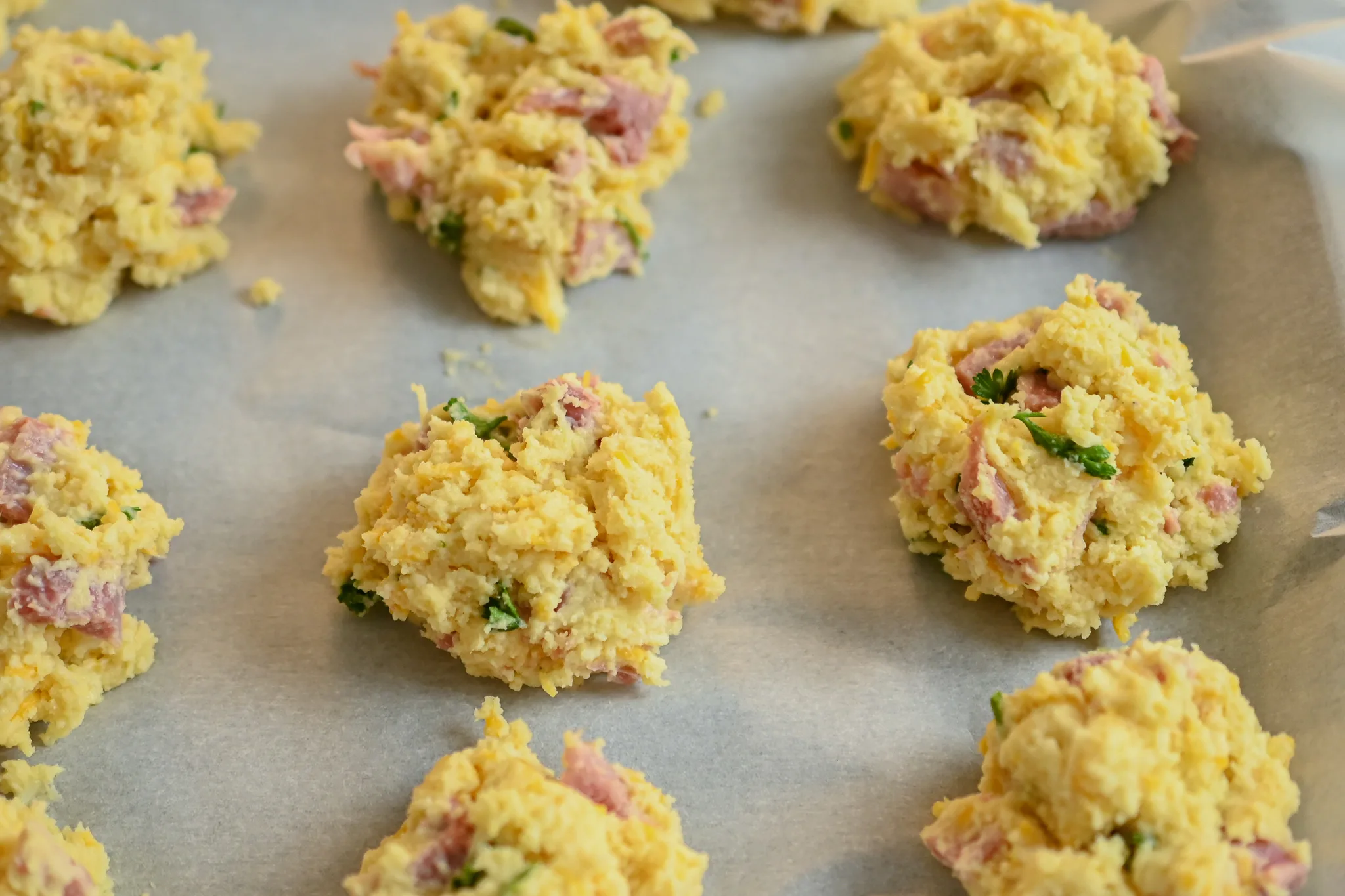 keto ham and cheese drop biscuits on baking sheet and parchment ready for the oven