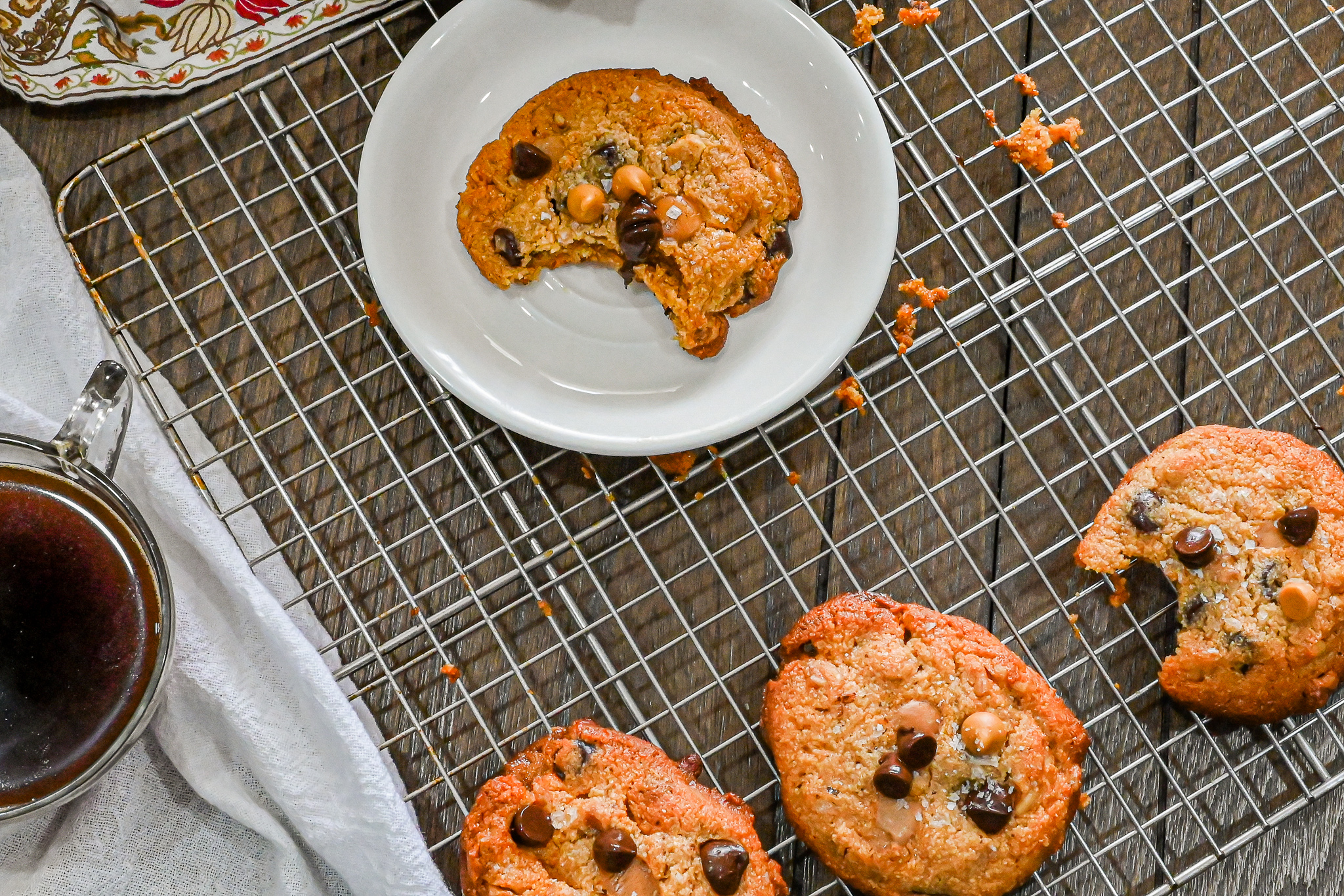 keto chocolate chip butterscotch cookies on cooling rack and bitten on white plate