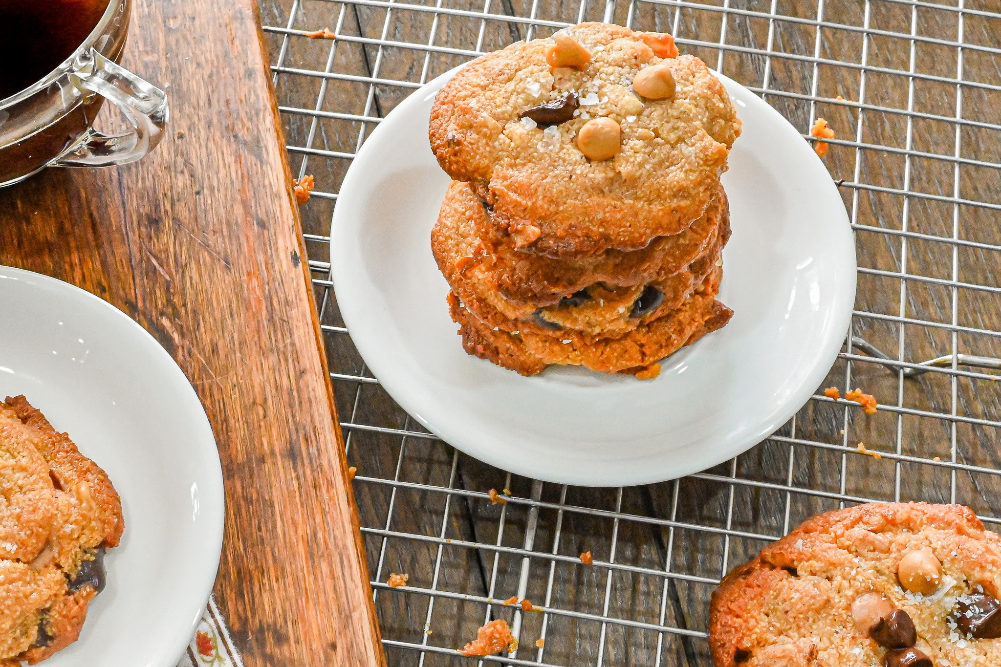 keto chocolate chip butterscotch cookies stack on small white plate with cooling rack in background