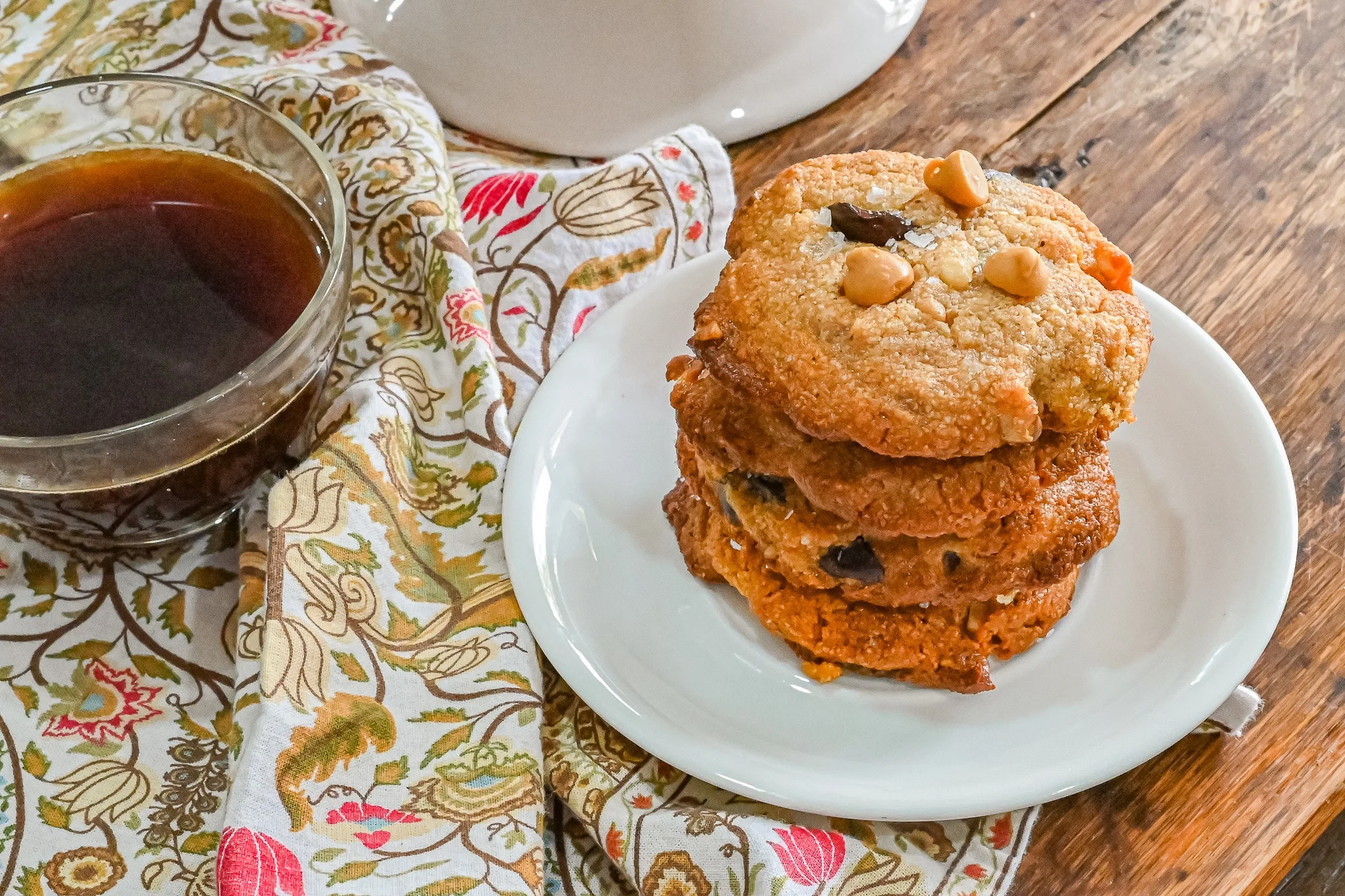 keto chocolate chip butterscotch cookies stack on white plate with coffee to the left