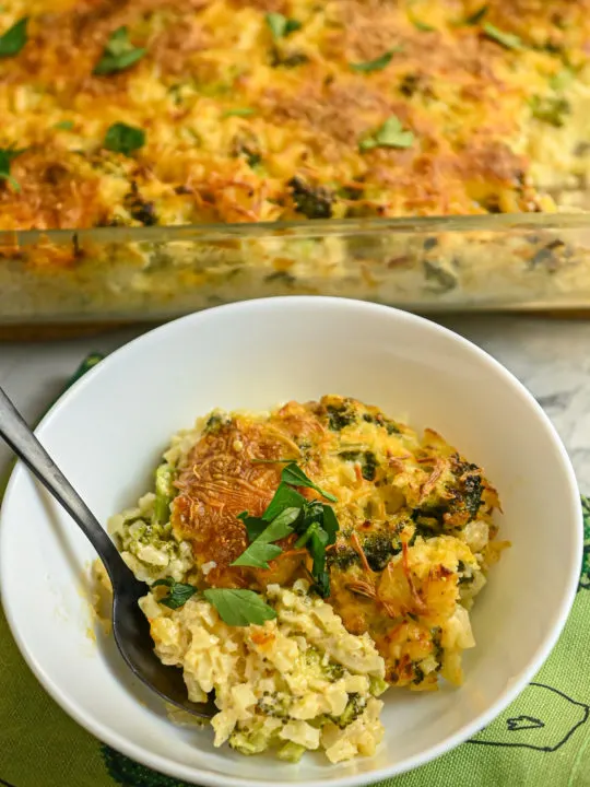 keto broccoli cauliflower rice casseroleserved in small white bowl with casserole dish in thr background