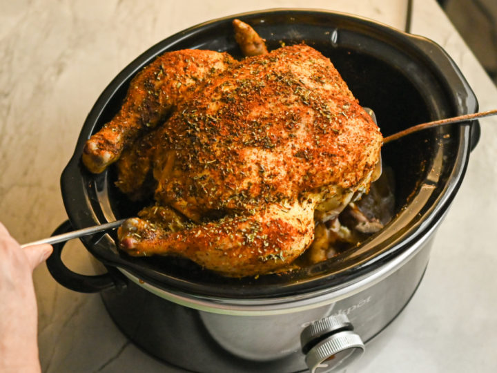 keto whole chicken lifted out of a crockpot with two metal spatulas