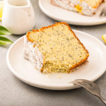 keto poppy lemon seed cake slice on a small white plate with lemon wedges next to it