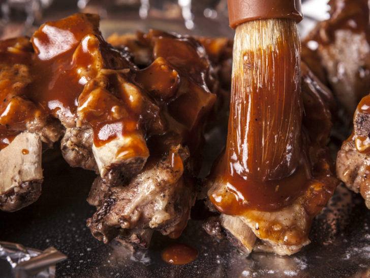 cooked ribs being based with sugar-free bbq sauce before placing them bake in the oven