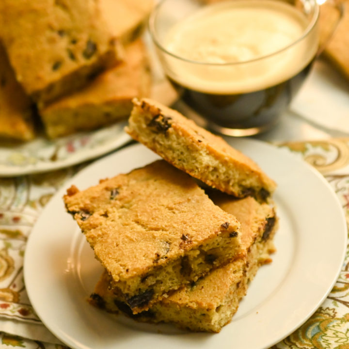 keto soft baked chocolate chip cookie bars stacked on a small white plate with coffee on the side