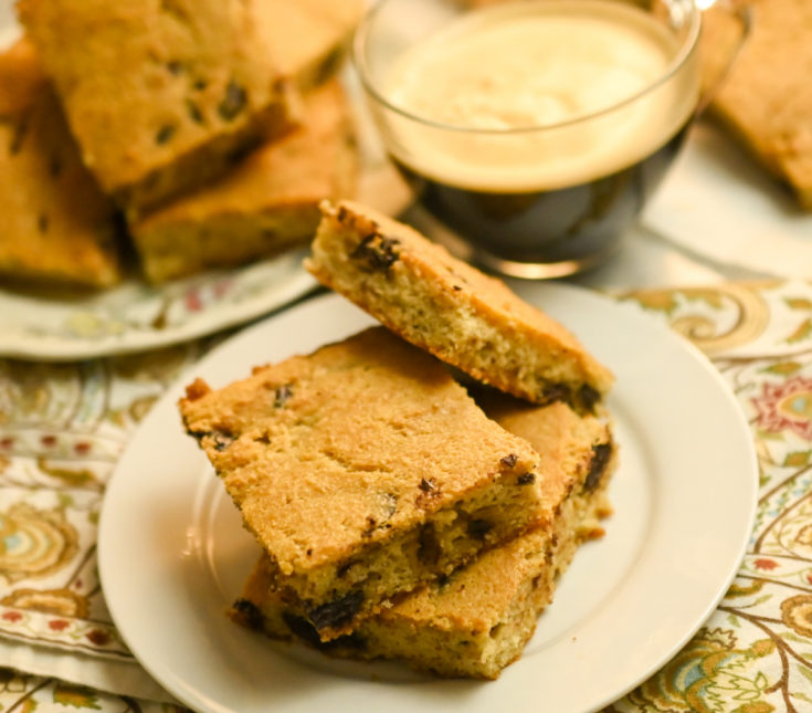 keto soft baked chocolate chip cookie bars stacked on a small white plate with coffee on the side