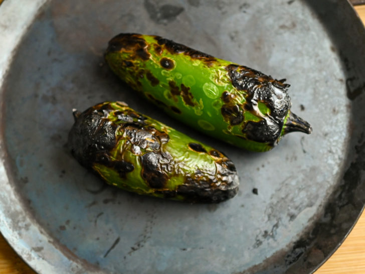 two whole roasted jalapeños on metal comal