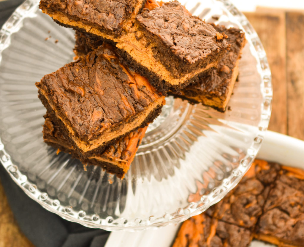 Keto pumpkin brownies stacked on a clear cake stand ready to enjoy