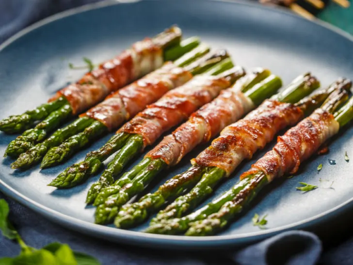 Keto bacon wrapped asparagus served in a bundle on a blue plate