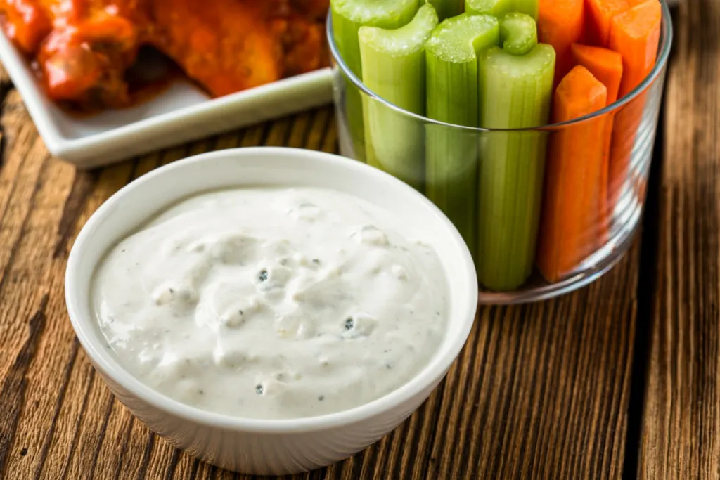 Low-carb blue cheese dip in a small white dish with carrot and celery sticks and buffalo wings