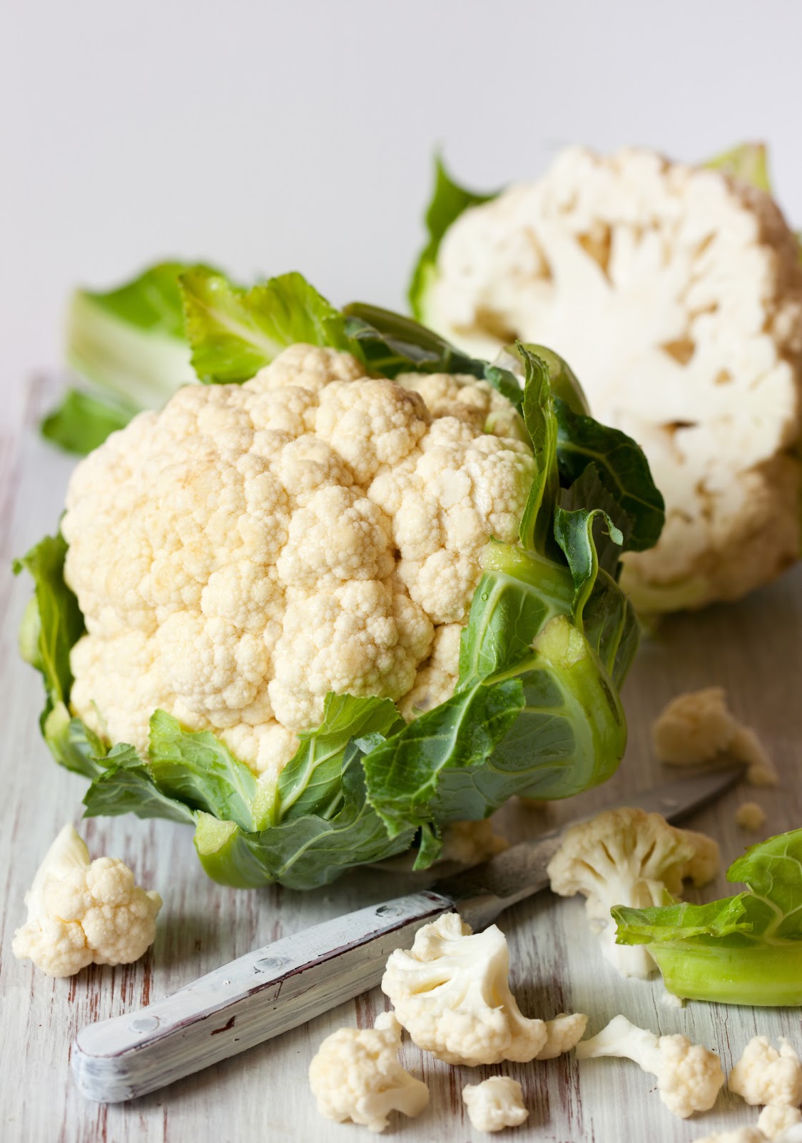 cauliflower being sliced on a white wooden board