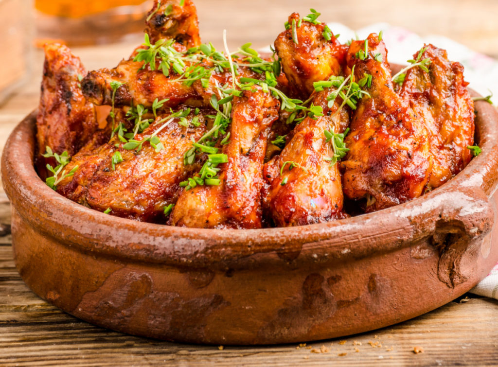 Keto jerk chicken wings served in an clay dish and garnished with fresh thyme and chopped scallions