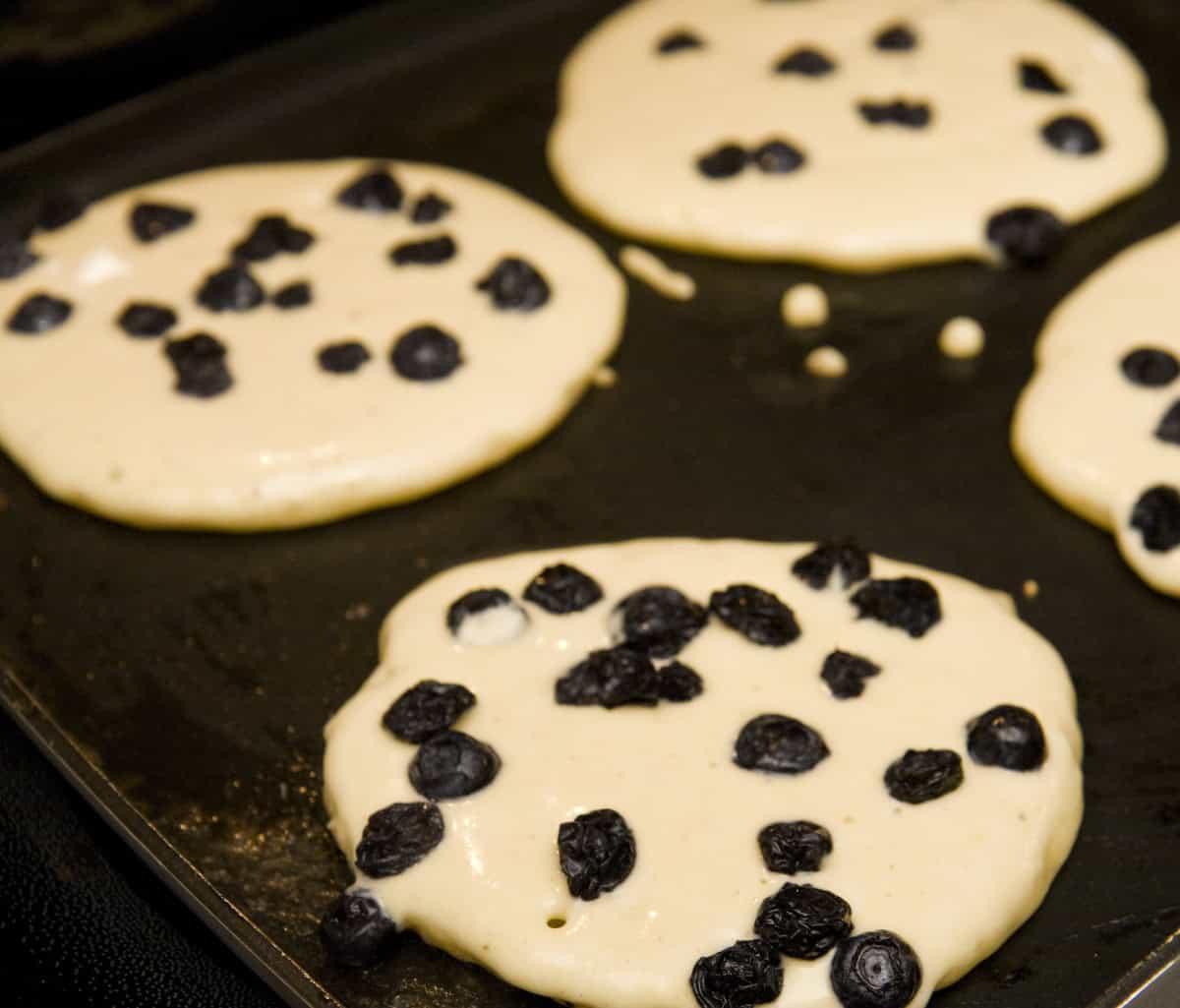 keto blueberry coconut flour pancakes being made on a griddle